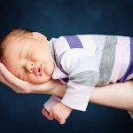 Portrait of newborn baby girl lying on father's arm by .