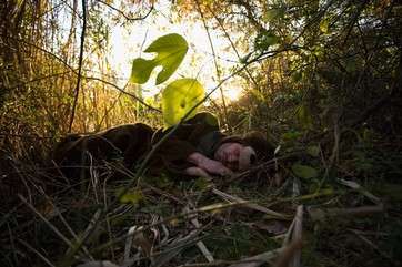 A man sleeping in woodland by . 