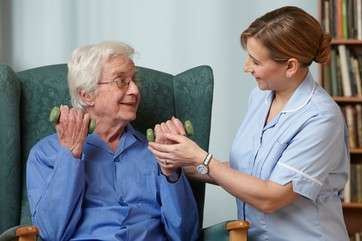 Carer assisting senior man with hand weights by . 